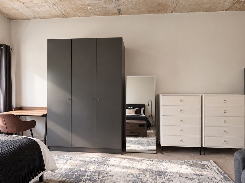 A well-lit bedroom featuring an exposed concrete ceiling and neutral tiled flooring, offering a modern industrial aesthetic.