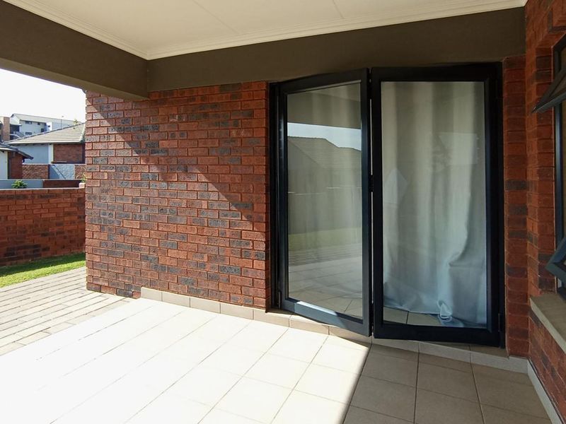 A covered patio area featuring exposed brick walls, tiled flooring, and modern aluminium-framed glass folding doors leading into the home.