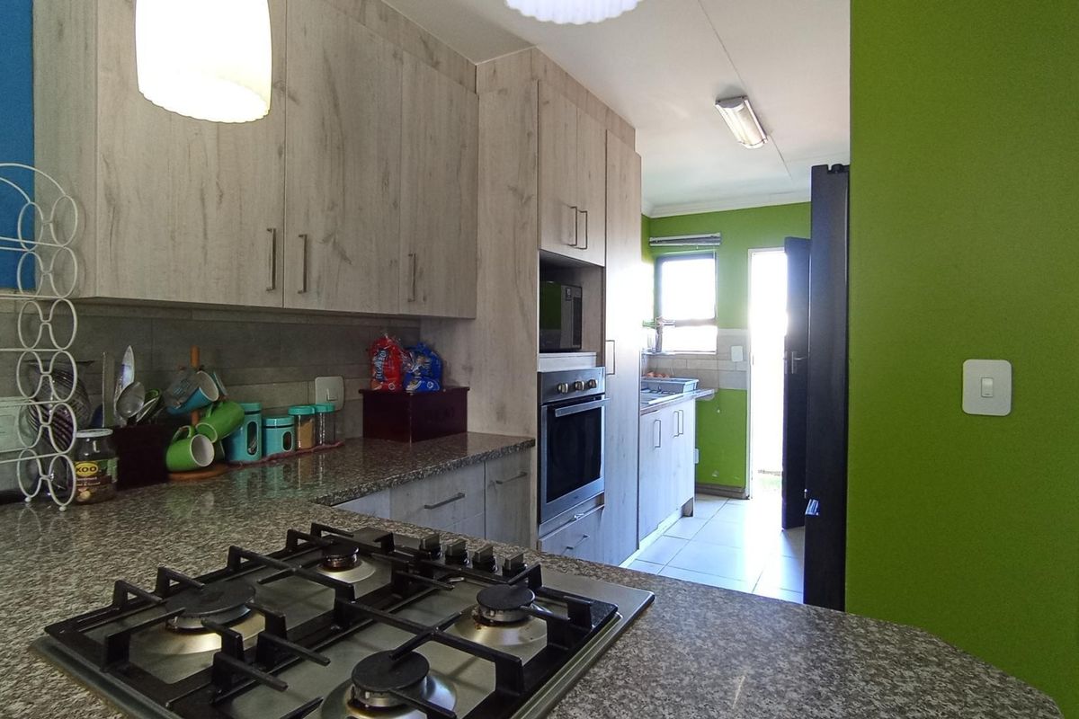 Functional kitchen featuring light wood-look cabinetry, granite countertops, a gas hob, and a built-in oven, with an adjacent scullery area.