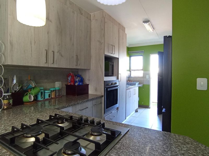Functional kitchen featuring light wood-look cabinetry, granite countertops, a gas hob, and a built-in oven, with an adjacent scullery area.