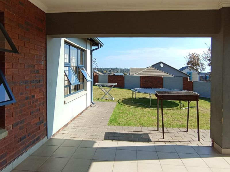 A covered patio area featuring tiled flooring and brick exterior walls, overlooking a private garden with paved pathways and boundary walling.