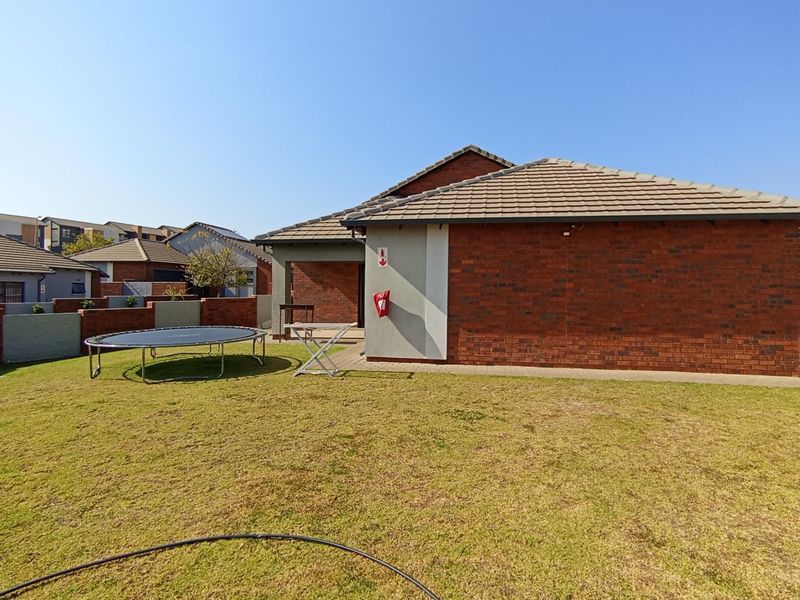 Rear view of the property featuring a brick facade, tiled roof, and a private garden with a paved patio area.