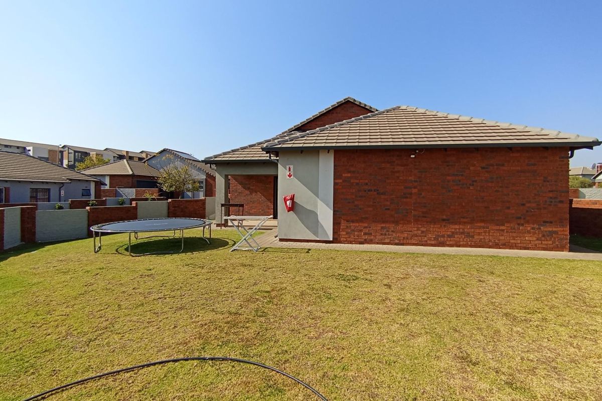 Rear view of the property featuring a brick facade, tiled roof, and a private garden with a paved patio area.