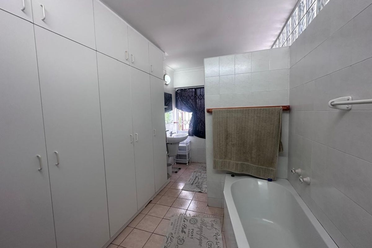 A functional bathroom featuring extensive built-in storage cabinetry, a standard bathtub, and a pedestal sink, finished with tiled surfaces and a glass block window.