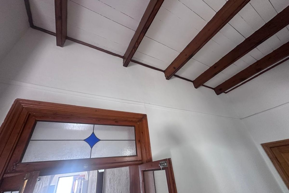 Interior view featuring high ceilings with exposed timber beams and a classic timber-framed door with a decorative stained glass transom window.