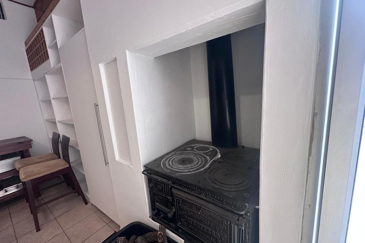 A kitchen area featuring a traditional cast iron wood-burning stove set into a built-in alcove with adjacent white shelving and tiled flooring.