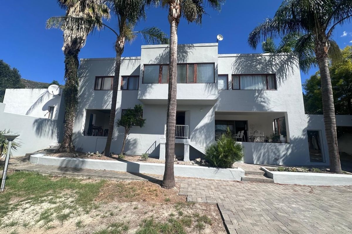 Rear elevation of a two-story house featuring a paved driveway, covered patio areas, and established palm trees.