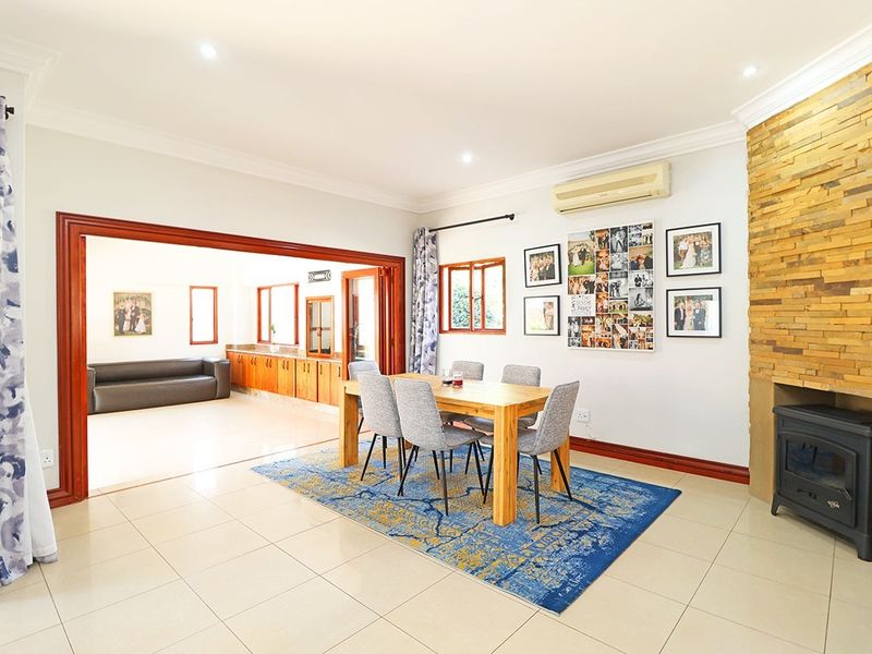 Spacious open-plan living and dining area featuring a stone-clad fireplace with a wood-burning stove, tiled flooring, and direct access to an adjacent room.