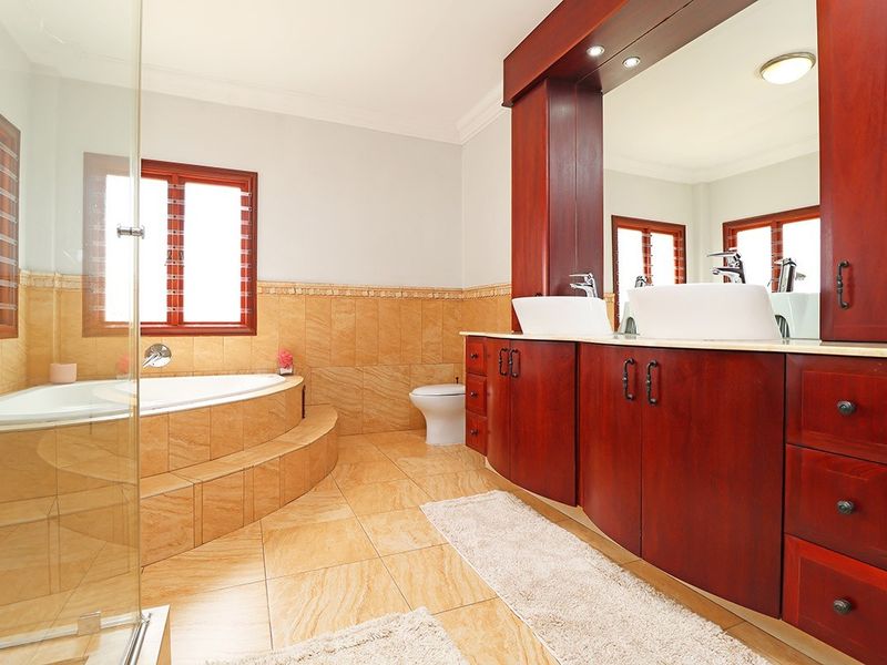 Spacious bathroom featuring a built-in vanity with double vessel sinks, a raised tiled bathtub, and a separate glass-enclosed shower area.