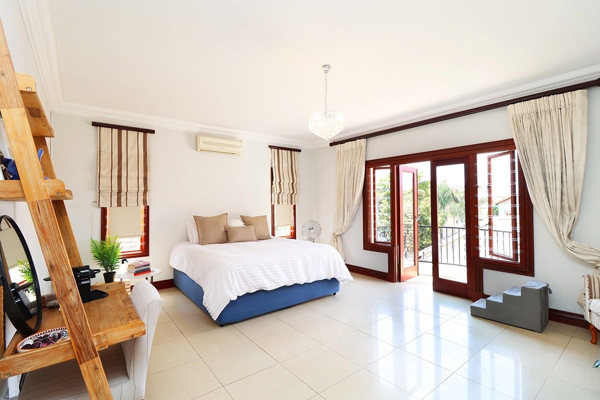 Spacious bedroom featuring tiled flooring, crown molding, a crystal chandelier, and double doors opening onto a private balcony.