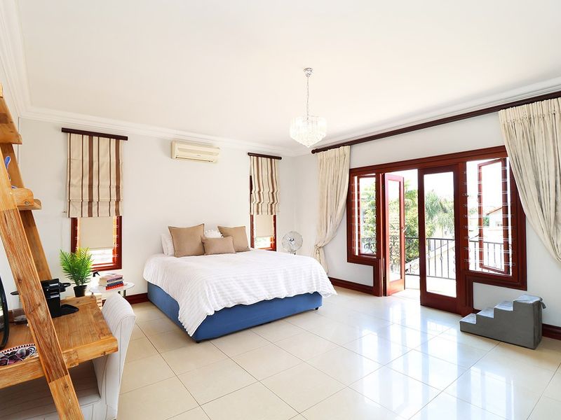 Spacious bedroom featuring tiled flooring, crown molding, a crystal chandelier, and double doors opening onto a private balcony.