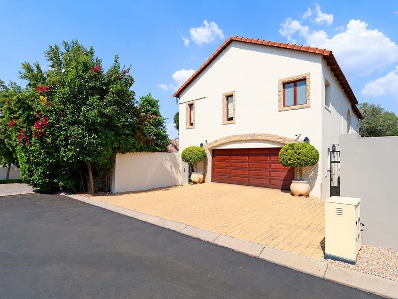 Front elevation of a well-maintained house featuring a paved driveway, double garage with a stone arch detail, and a secure perimeter wall.
