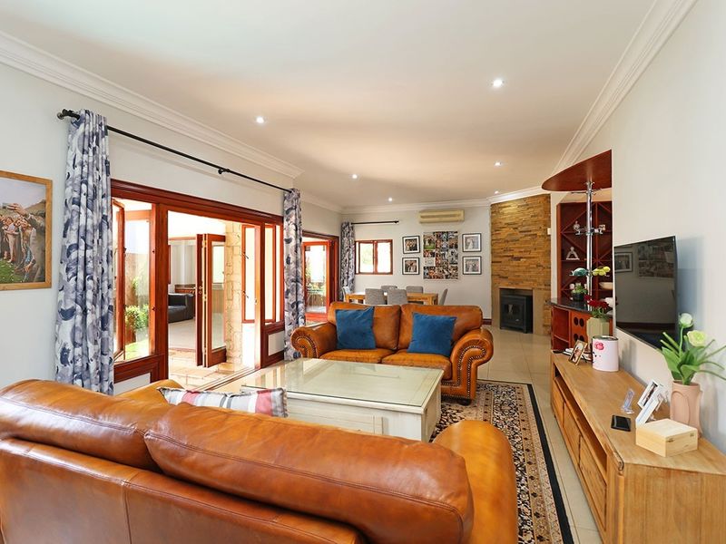 Spacious living room featuring a stone-clad fireplace, built-in bar, and large timber-framed doors opening to an outdoor area, finished with tiled flooring.