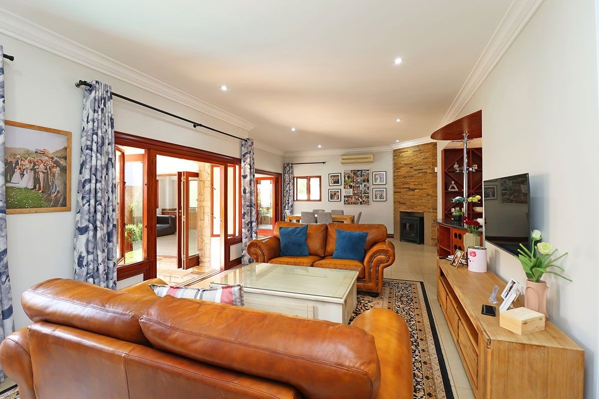 Spacious living room featuring a stone-clad fireplace, built-in bar, and large timber-framed doors opening to an outdoor area, finished with tiled flooring.