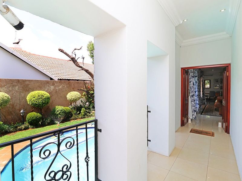 A covered patio area featuring tiled flooring and wrought iron railings, overlooking a swimming pool and garden space.
