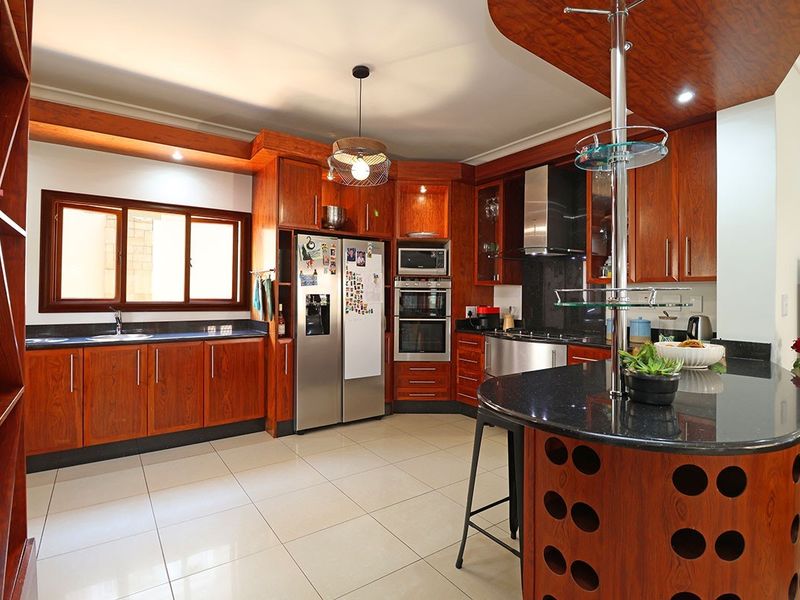 Spacious kitchen featuring warm wooden cabinetry, granite countertops, built-in appliances, and a functional breakfast bar with tiled flooring throughout.