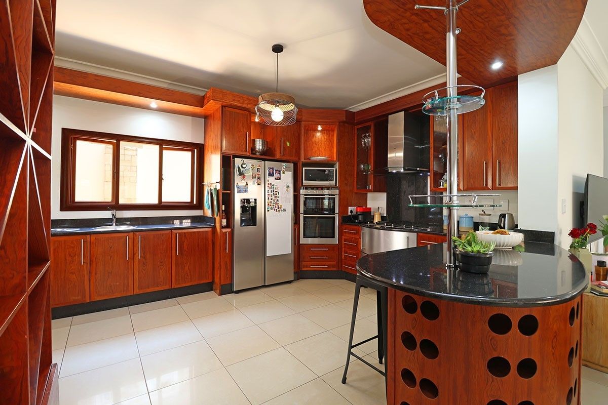 Spacious kitchen featuring warm wooden cabinetry, granite countertops, built-in appliances, and a functional breakfast bar with tiled flooring throughout.
