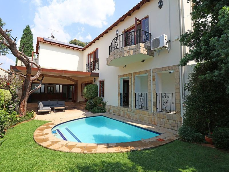 Rear exterior view featuring a swimming pool, stone-clad facade, wrought iron balcony railings, and a covered patio area.