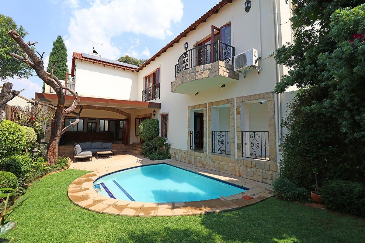Rear exterior view featuring a swimming pool, stone-clad facade, wrought iron balcony railings, and a covered patio area.