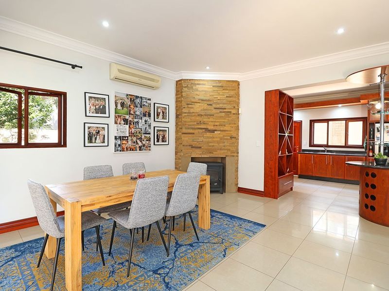 Spacious open-plan dining and kitchen area featuring a stone-clad fireplace, wood-burning stove, tiled flooring, and custom wooden cabinetry with a central island.