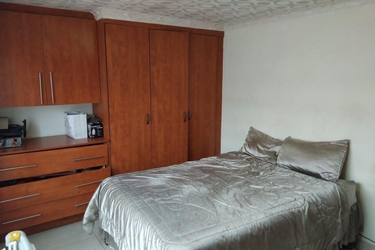 A bedroom featuring built-in wooden cupboards, tiled flooring, and a patterned ceiling, offering functional storage space.