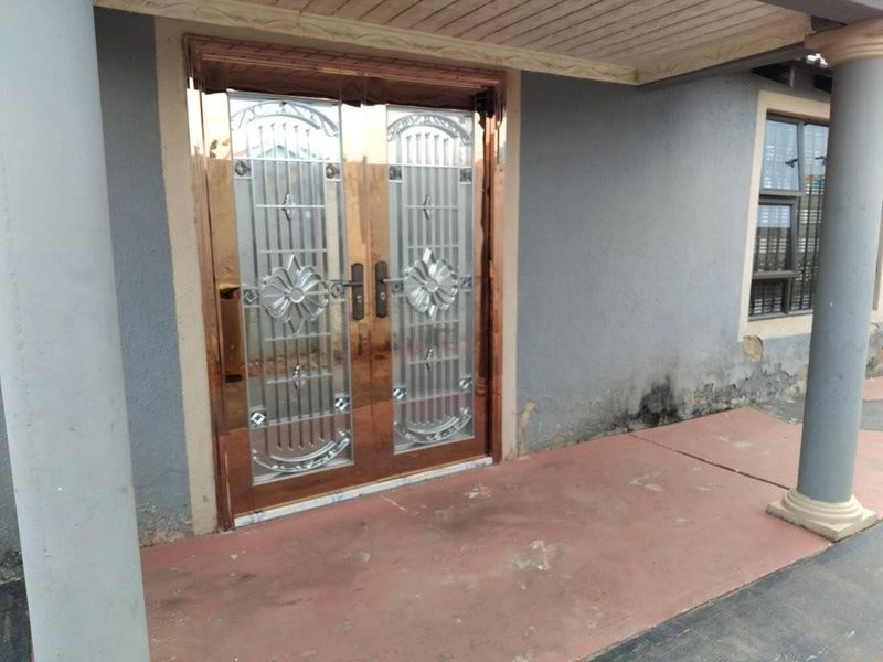 Front entrance area featuring a decorative metal security gate, double doors, and a covered patio with visible exterior wall maintenance required.