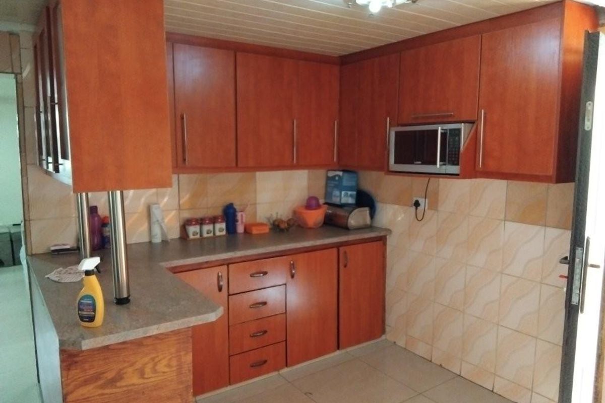 A functional kitchen featuring wood-look laminate cabinetry, tiled backsplash, and built-in microwave space, offering a practical layout with potential for modern cosmetic updates.