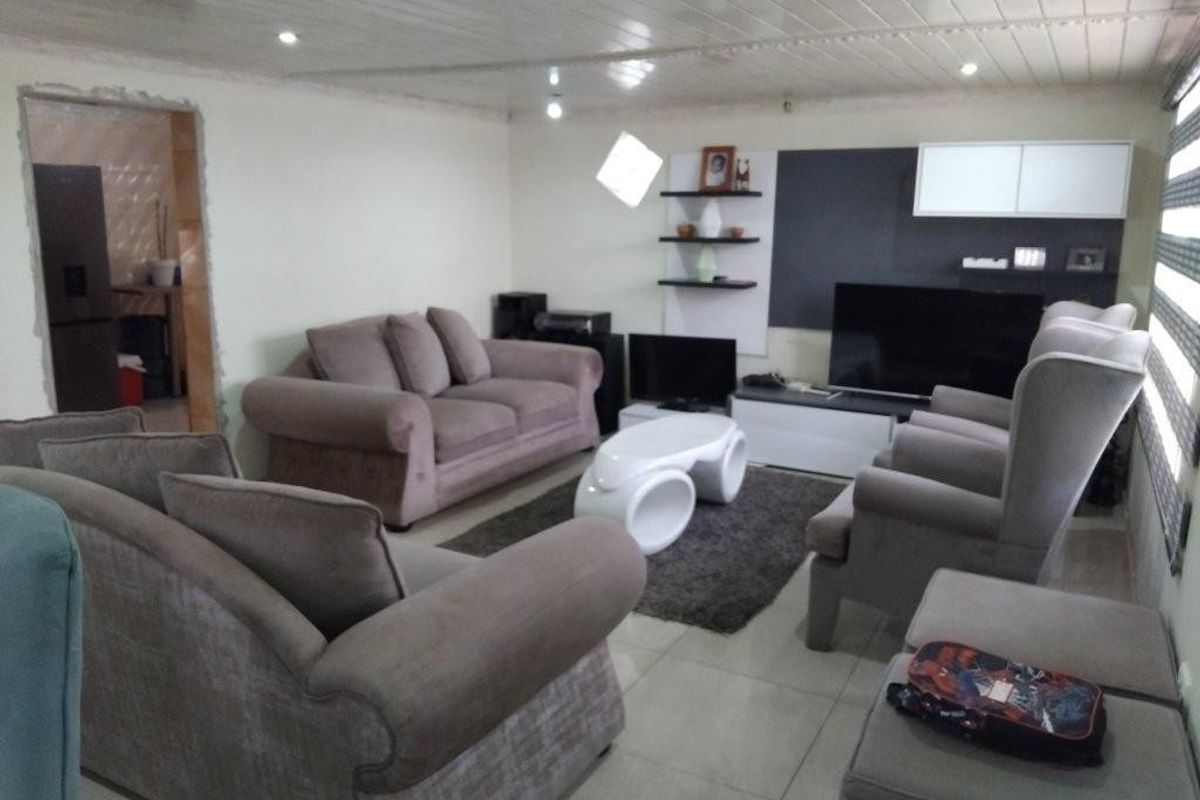 A living room featuring tiled flooring, recessed downlighting, and a built-in shelving unit, with an adjacent doorway leading to another room.