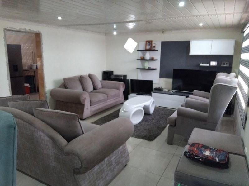 A living room featuring tiled flooring, recessed downlighting, and a built-in shelving unit, with an adjacent doorway leading to another room.