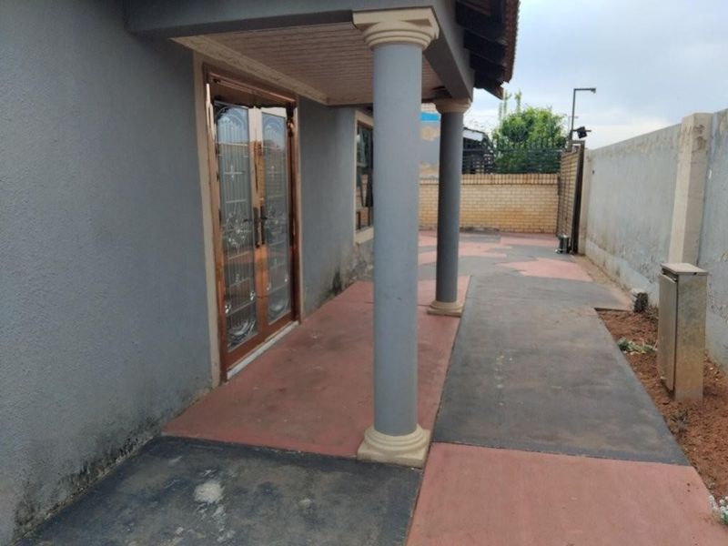 A covered outdoor patio area featuring concrete columns, paved flooring, and a secure entrance door, providing a functional space for outdoor living.