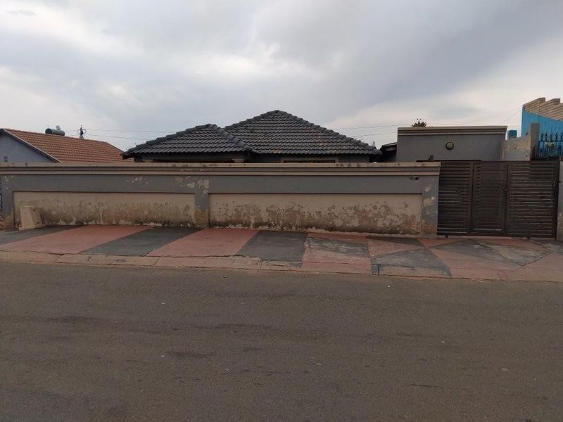 Front exterior view of the property featuring a tiled roof, a gated entrance, and a perimeter wall with visible wear and weathering.