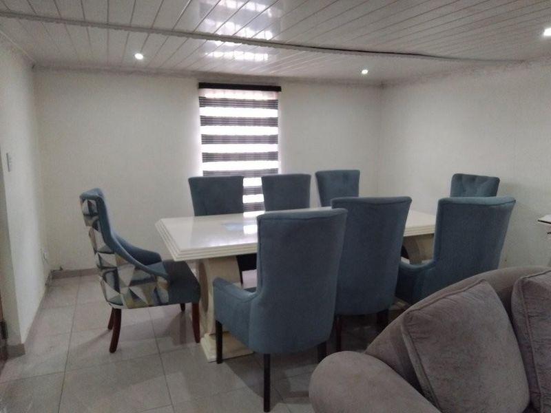 A dining room featuring tiled flooring, slatted ceiling panels with recessed lighting, and a window fitted with a modern roller blind.