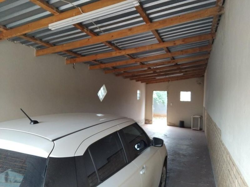 A functional garage space featuring exposed timber rafters, corrugated metal roofing, and concrete flooring with access to the rear exterior.