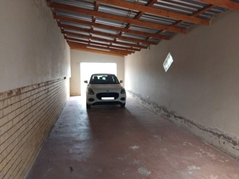 A long, covered garage space featuring exposed timber rafters, corrugated roofing, and brick wall detailing with concrete flooring.