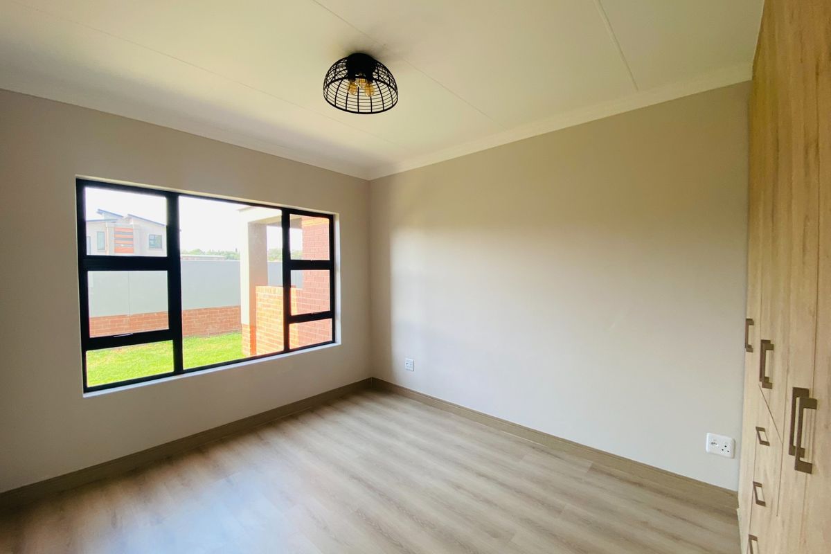 A bright, modern bedroom featuring neutral walls, light wood-look laminate flooring, and built-in cupboards with contemporary hardware.