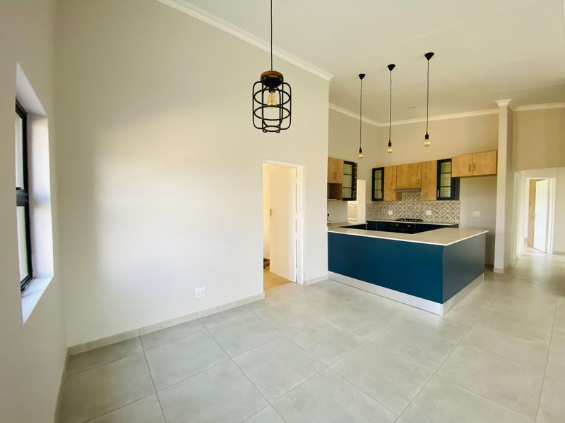 Modern open-plan kitchen and living area featuring contemporary cabinetry, stone countertops, stylish pendant lighting, and neutral tiled flooring throughout.