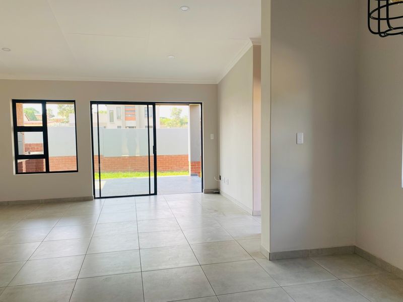 Bright and spacious open-plan living area featuring neutral tiled flooring, recessed lighting, and large sliding glass doors leading to an outdoor patio.
