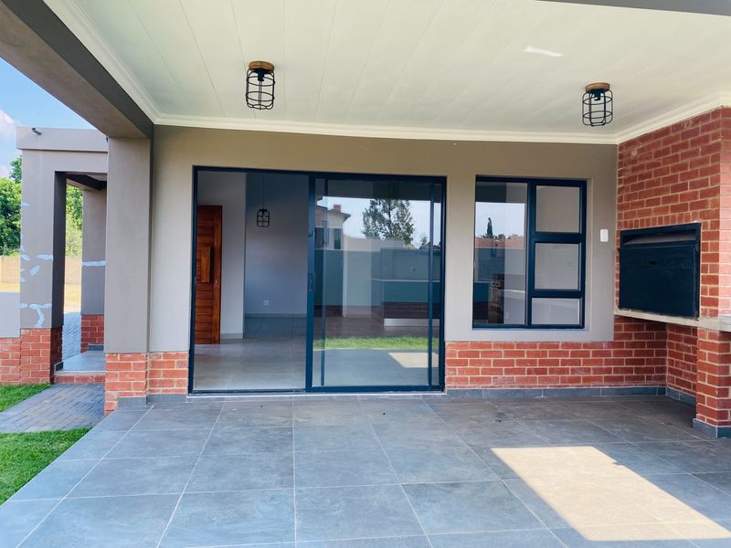 Covered patio area featuring a built-in braai, tiled flooring, and sliding glass doors providing seamless access to the interior living space.