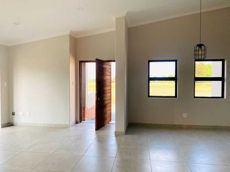 A bright, open-plan living area featuring neutral tiled flooring, modern pendant lighting, and large windows that provide ample natural light.