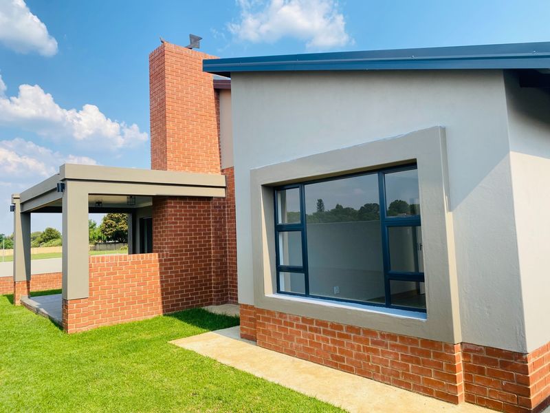 Rear view of the property featuring a modern brick and plaster facade, covered patio area, and large aluminium-framed windows overlooking the garden.