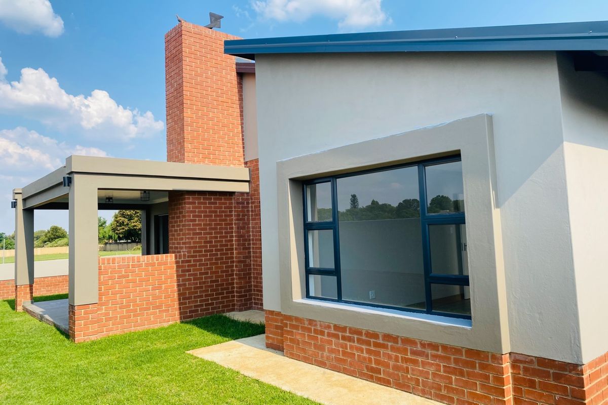 Rear view of the property featuring a modern brick and plaster facade, covered patio area, and large aluminium-framed windows overlooking the garden.