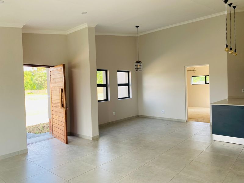 Spacious open-plan living area featuring neutral tiled floors, modern pendant lighting, and a contemporary kitchen island, offering a bright and versatile layout.