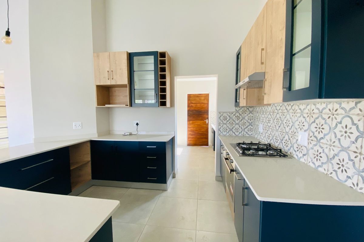 Modern kitchen featuring two-tone cabinetry, quartz countertops, patterned tile backsplash, and integrated gas hob with oven, offering a clean and contemporary aesthetic.