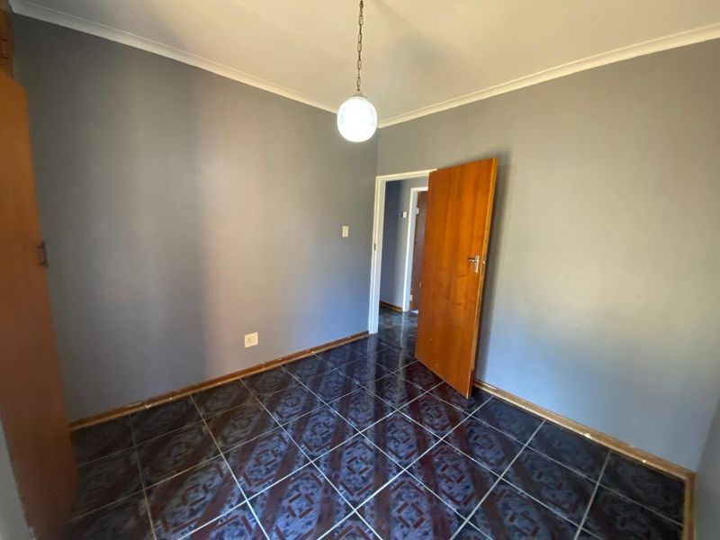 An empty bedroom featuring dark patterned floor tiles, grey walls, and a simple pendant light fixture.