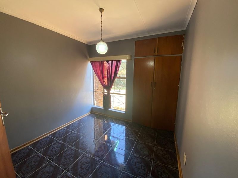 A clean, empty bedroom featuring dark tiled flooring, built-in wooden cupboards, and security bars on the window.