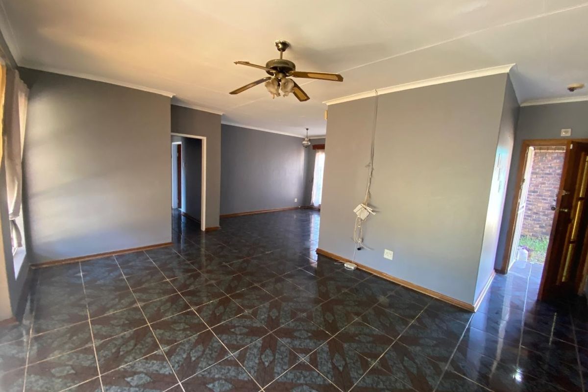 An empty, open-plan living area featuring dark patterned floor tiles, grey walls, and a ceiling fan, with an external door leading to the side yard.