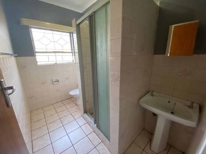A functional bathroom featuring a pedestal basin, shower enclosure, and toilet, finished with dated wall and floor tiling.