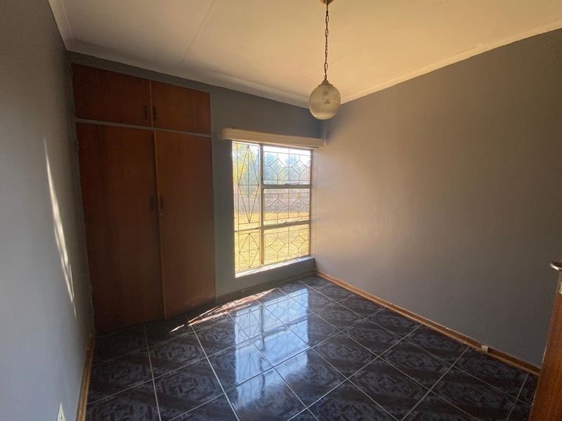 A vacant bedroom featuring dark tiled flooring, built-in wooden cupboards, and a window fitted with security bars.