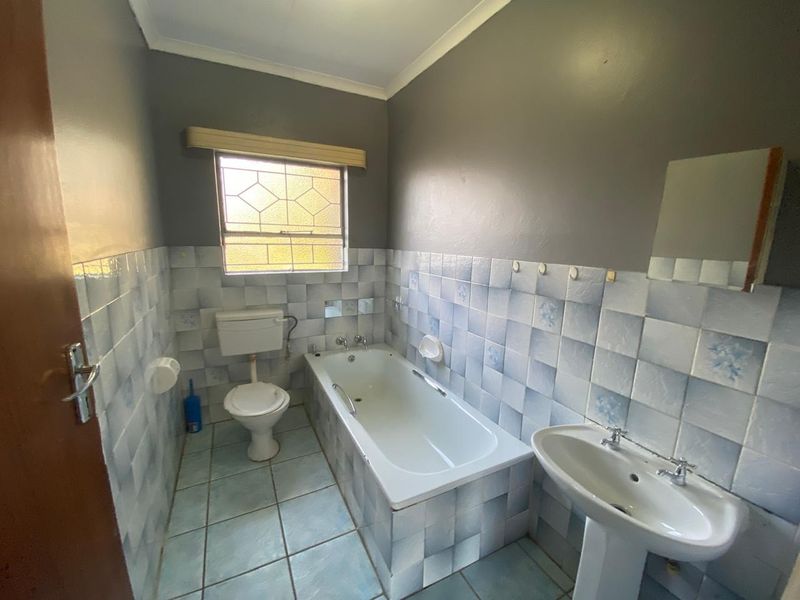 A functional bathroom featuring a bathtub, pedestal basin, and toilet, finished with dated wall and floor tiling.