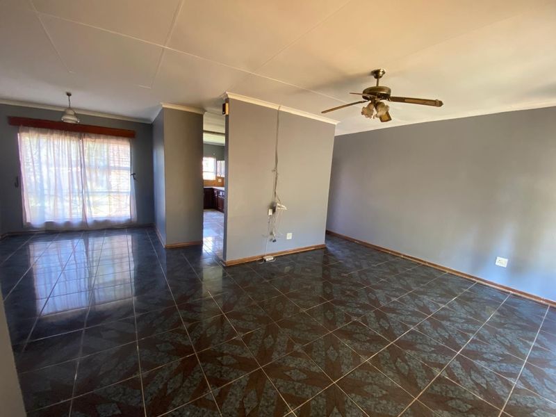 An open-plan living area featuring dark patterned floor tiles, a ceiling fan, and neutral grey walls, offering a blank canvas for interior design.